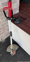 Full view of red and black cordless weed eater with attached battery, showing aluminum shaft and handle.