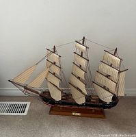 Full view of the Fragata ship model showing three masts with striped sails, rigging details, black and red hull, and wooden base.