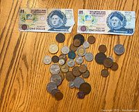 Two Central Bank of the Bahamas $1 bills with various world coins scattered below on a wooden surface.