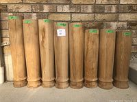 Eight oak columns lined up vertically with green tape labels indicating various heights: 23, 27, 23 3/4, 23 1/2, 23 7/8 inches. Columns have a 6-inch diameter and a natural wood finish.