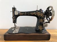 Full side view of the entire antique Singer hand crank sewing machine showing floral decorations, hand crank wheel, and wooden base.