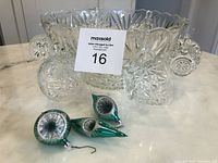 Photo showing large crystal punch bowl surrounded by six crystal cups and three green Christmas ornaments on a countertop.