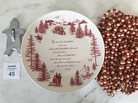 Ceramic cookie plate with Christmas red design and wooden bead garlands coiled beside it, along with gingerbread cookie cutter.