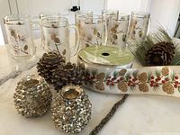 Image showing the full lot with all eight clear glass beer steins decorated with gold pinecones and pine needles, four metallic pinecone candle holders, roll of pinecone wire ribbon, and faux pine branch with pinecone
