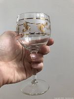 Close-up of a single vintage Libby wine glass held in hand showcasing gold pinecone and leaf design around upper bowl.