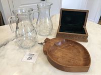 Set of two clear glass pitchers, wooden peach bowl, and carved wooden box displayed on white marble surface