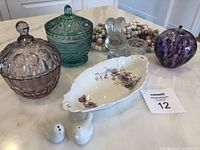 View of all items in the lot showing three decorative glass candy dishes, ceramic bird-shaped salt and pepper shakers, floral serving bowl, clear glass bunny figurine, purple glass orb, and bead garlands.