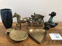 Photo of all six items together showing the brass horse and buggy figurine, pineapple tray, heart-shaped spade tray, and three Blue Mountain Pottery pieces: blue vase, green bunny, and green duck, displayed on a wood surface.
