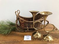 Photo showing entire set: brass candlestick holders shaped like horn instruments, wooden bark sleigh, and faux greenery sprig on wooden surface.