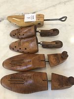 Three vintage wooden shoe forms and stretcher laid out on a marble surface, showing the different sizes, shapes, and metal handles.