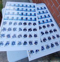 Two uncut sheets of 2004 Toronto Maple Leafs hockey cards displayed on a table against a brick wall. Each sheet contains multiple cards showing player images, names, and stats. The sheets show minor signs of wear.