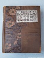 Front cover of the antique book 'The Boys Own Indoor Book' showing floral cloth design and embossed metallic title plate.