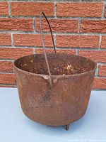 Side view of the heavily rusted antique cast iron pot cauldron showing metal handle and three feet for stability.