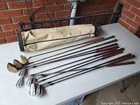 Full set of golf clubs including irons, woods, and putter arranged on a table with the canvas bag to the side, showing the complete lot.