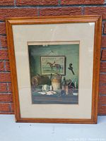 Front view of antique print in tiger maple frame leaning against brick wall.