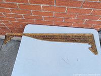 Cast iron embossed metal sign component laid horizontally on a white surface against a brick wall. Shows full length of ornate sign with clear embossed text.