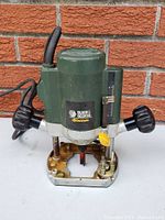 Front view of Green Black & Decker Quantum router showing brand label, depth gauge, knobs, and base plate.