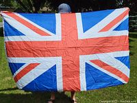 British flag held outdoors against greenery, showing the full Union Jack design with some wrinkling in the fabric.