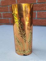 Front view of tall copper vase showing embossed leaf design and polished surface with some wear.