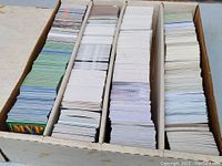 Large lot of sports cards stacked and sorted in a long white cardboard box with multiple internal dividers to separate stacks of cards.
