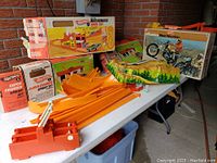 Four vintage Hot Wheels track sets displayed on a table with original boxes including mountain-themed set and orange track pieces.