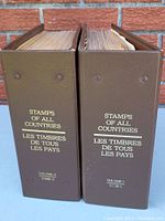 Two large brown binders side by side, labeled 'Stamps of All Countries' in English and French, with volume numbers 1 and 11.