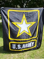Full view of large black U.S. Army flag banner held up outdoors showing star logo and 'U.S. ARMY' text.