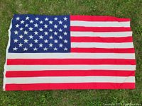 Full display of the vintage USA flag with 49 stars and 13 stripes laid flat on grass.