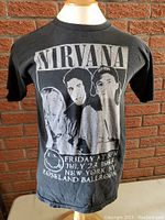 Front view of the black Nirvana vintage T-shirt on a mannequin against a brick wall.