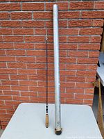 Fishing pole extended next to metal storage case against a brick wall.