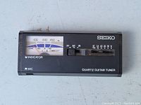 Front view of black Seiko quartz guitar tuner showing analog meter with frequency and cent scale, power switch and battery check.