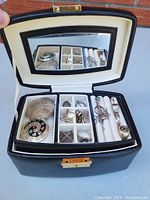 Open jewelry box with mirror showing multiple sections of rings, brooches, pendants, and cufflinks in various silver designs and styles.