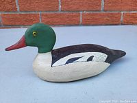 Clear angled side view of vintage carved duck decoy showing painted green head and red bill
