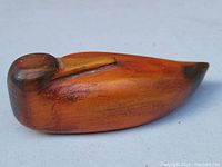 Side view of carved duck figure showing brown cedar wood with darker head and tail accents.