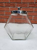 Front and side view of the clear glass vintage cookie jar with metal lid, showing the hexagonal shape and design details.