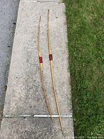 Two long wooden bows laid out on the ground showing full length and leather-wrapped grips.
