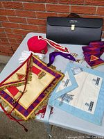 Overview photo of the Masonic collection including robe, gloves, aprons, cap, medals, sash, coin, and cases.