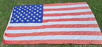 Full view of vintage American flag flat on grass showing full 50 stars and full stripes.