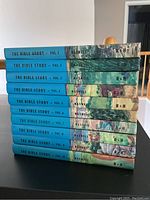 Side view of 10 volumes of 'The Bible Story' by Maxwell, showing blue spines with title and author details.