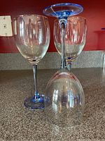 Three clear wine glasses with vibrant blue stems and bases shown on a countertop, one glass upside down in front