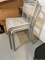 Four white outdoor chairs with silver metal frames stacked together.