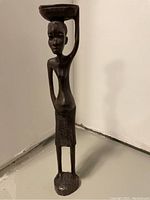 Front view of the carved wooden African woman statue showing detailed facial features and the bowl on her head.