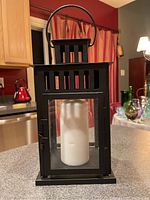 Front view of black metal lantern with glass panels and white pillar candle inside on kitchen counter.