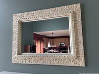 Full view of the large rectangular mirror with ornate white decorative frame hung on a wall.