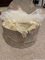 Photo of tulle veil and decorated headpiece inside the original floral patterned round storage box.