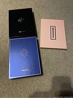 All three closed album boxes on a carpeted floor; black Reality In Black box, blue Blue album, and pink debut album box