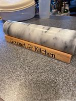 Marble rolling pin without handles placed on wooden stand with 'Gourmet Kitchen' branding on a countertop.