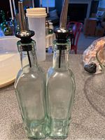 Front view of two clear rectangular glass oil dispensers with metal pour spouts on a kitchen counter.