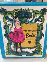 Photo of outside of blue Barbie doll case with colorful decorative graphics showing 'The World of Barbie' and floral design, featuring Barbie illustration.