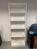 Front view of the tall white bookshelf with five shelves, showing surface wear and scratches on shelves and sides.